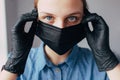 A nurse dressing a black mask and medical gloves and looking in the camera and thinks how to protect people from the coronavirus.