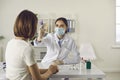 Nurse in face mask measuring woman`s body temperature with non-contact thermometer Royalty Free Stock Photo