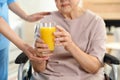 Nurse giving glass of juice to elderly woman indoors. Assisting senior people Royalty Free Stock Photo