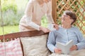 Nurse giving tea to happy elderly woman reading book on the terr Royalty Free Stock Photo