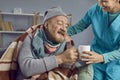 Nurse taking care of a sick retired senior man, helping him and making him hot tea