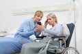 Nurse helps with cell phone to contact the elderly lady`s family in the wheelchair near bed in hospital room, concept of Royalty Free Stock Photo