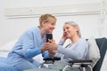 Nurse helps with cell phone to contact the elderly lady`s family in the wheelchair near bed in hospital room, concept of Royalty Free Stock Photo