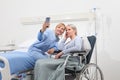 Nurse helps with cell phone to contact the elderly lady`s family in the wheelchair near bed in hospital room, concept of Royalty Free Stock Photo