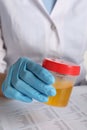 Nurse holding container with urine sample for analysis at table, closeup Royalty Free Stock Photo