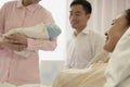 Nurse holding newborn baby in the hospital with mother lying on the bed and the father beside her Royalty Free Stock Photo