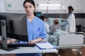 Nurse at medical desk typing patient data into computer while team of doctors putting iv drip line