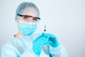 Nurse in a medical gown, mask and protective gloves with transparent glasses on her face with a syringe in her hands