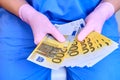 A nurse in a medical uniform is counting money in euro notes, close-up. The concept of the salary of doctors in Europe, the