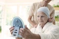 Nurse and patient with cancer wearing headscarf and looking at the mirror.