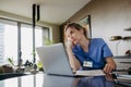 Nurse paying bills online, sitting in living room, working on notebook. Doctor in scrubs dealing with work issues from Royalty Free Stock Photo