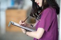 Nurse in purple uniform standing at patient room and writing