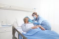 Nurse puts oxygen mask on elderly woman patient lying in the hospital room bed, wearing protective gloves and visor medical mask, Royalty Free Stock Photo