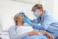 Nurse puts oxygen mask on elderly woman patient lying in the hospital room bed, wearing protective gloves and visor medical mask, Royalty Free Stock Photo