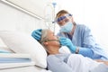 Nurse puts oxygen mask on elderly woman patient lying in the hospital room bed, wearing protective gloves and visor medical mask, Royalty Free Stock Photo