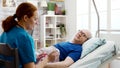 Nurse in retirement home giving prescription pills to a sick lying in hospital bed man