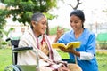 Nurse and senior woman on wheel chair laughing by reading book or novel at park - concept of relaxation, professional Royalty Free Stock Photo