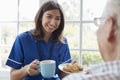 Nurse serves tea and biscuits to senior, over shoulder view Royalty Free Stock Photo