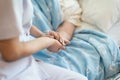 Nurse sitting on a hospital bed next to an older woman helping hands, care for the elderly concept