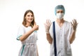 A nurse stands next to a doctor in a medical mask, a cap and sterile gloves and happily points up