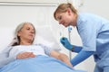 Nurse with the syringe injects the vaccine to the elderly woman patient lying in the hospital room bed