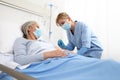 Nurse with the syringe injects the vaccine to the elderly woman patient lying in the hospital room bed, wearing protective gloves Royalty Free Stock Photo