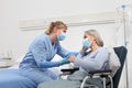 Nurse take comfort elderly woman in wheelchair wearing surgical protective medical masks in hospital room, concept of isolation