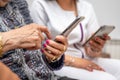 Nurse teaching elder woman how to use mobile phone, senior grandmother learning to use smartphone at nursing home