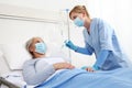 Nurse with thermometer measures fever on elderly woman patient lying in the hospital room bed, wearing protective gloves and Royalty Free Stock Photo