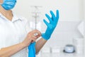 A nurse in a white coat puts on rubber gloves before a medical procedure in a bright handling room Royalty Free Stock Photo