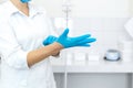 A nurse in a white coat puts on rubber gloves before a medical procedure in a bright handling room