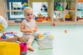 Nursery school. Toddler girl playing with different plastic toys such as building blocks, car toys, playhouses. Work on