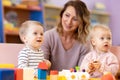 Nursery teacher looking after children in daycare. Little kids toddlers play together with developmental toys Royalty Free Stock Photo