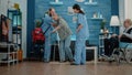 Nurses helping disabled pensioner to use walk frame