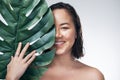 Nurture your skin the natural way. Studio shot of a beautiful young woman holding a monstera leaf against her face.