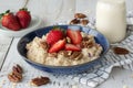 Nutritious oatmeal bowl with fresh strawberries, nuts and milk on white wooden table