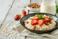 Nutritious oatmeal bowl with fresh strawberries, nuts and milk on white wooden table