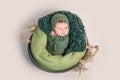 Nwborn swaddled in green coccon lying on basket