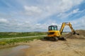 Colorful yellow digger stands on sandy ground in front of vivid blue sky