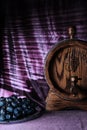 Oak barrel with wine and grapes out of focus on purple velvet background with light and shadow pattern