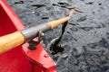Oar is held on an oarlock attached to a red boat, against the background of water.