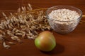 Oat ears stems and oat flakes and green apple in a bowl on a dark brown wood background. oat flakes big size grind. Useful fiber-