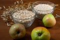 Oat ears stems and oat flakes and green apples in a bowl on a dark brown wood background. oat flakes big and small size grind.