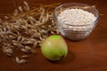 Oat ears stems and oat flakes and green apple in a bowl on a dark brown wood background. oat flakes small size grind. Useful fiber