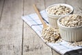 Oat flakes in ceramic bowls and wooden spoon on linen napkin, golden wheat ears on rustic wooden background Royalty Free Stock Photo