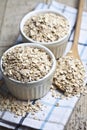 Oat flakes in ceramic bowls and wooden spoon on linen napkin, golden wheat ears on rustic wooden background Royalty Free Stock Photo