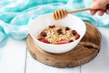 Oat grain cereal with berries and honey in a white plate on a wooden table