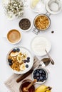 Oat granola with yogurt, honey, fresh bananas, blueberries, chia seeds in bowl and cup of coffee on white background