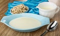 Oat rings in bowl on napkin, jug with yogurt, blue bowl with yogurt, spoon on wooden table