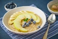 Oatmeal with bananas, blueberries, jam, honey, blue napkin on blue stone background. Close-up, side view